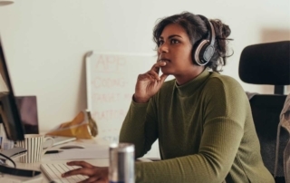 Photo of a woman looking at her computer screen while wearing her headphones and considering the scope of the gender pay gap in technology.