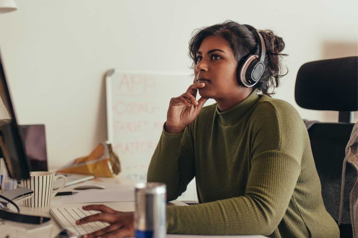 Photo of a woman looking at her computer screen while wearing her headphones and considering the scope of the gender pay gap in technology.