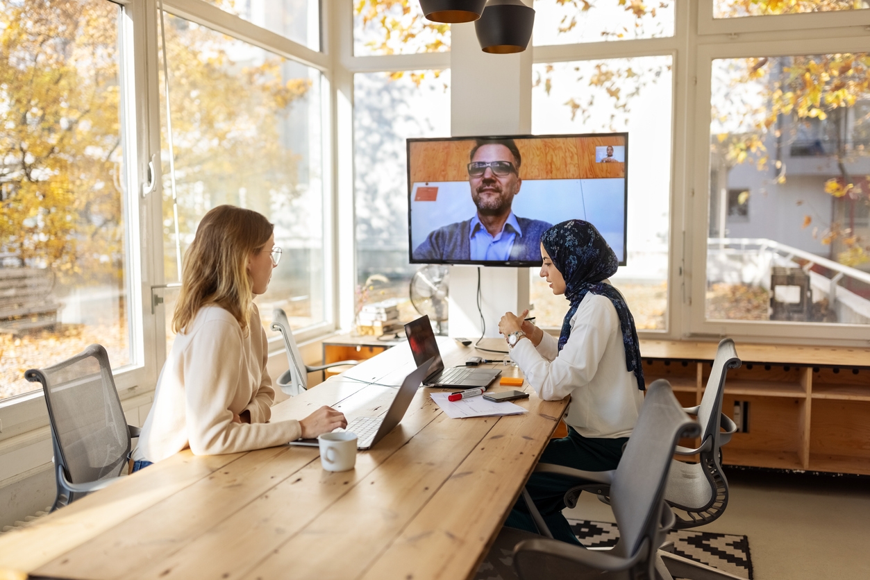 Two female entrepreneurs working in a hybrid workplace with their male colleague using video conferencing to attend the meeting.